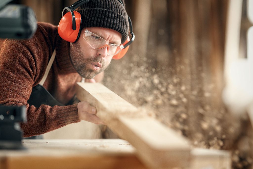 Zimmermann pustet Späne von einem Holzstück
